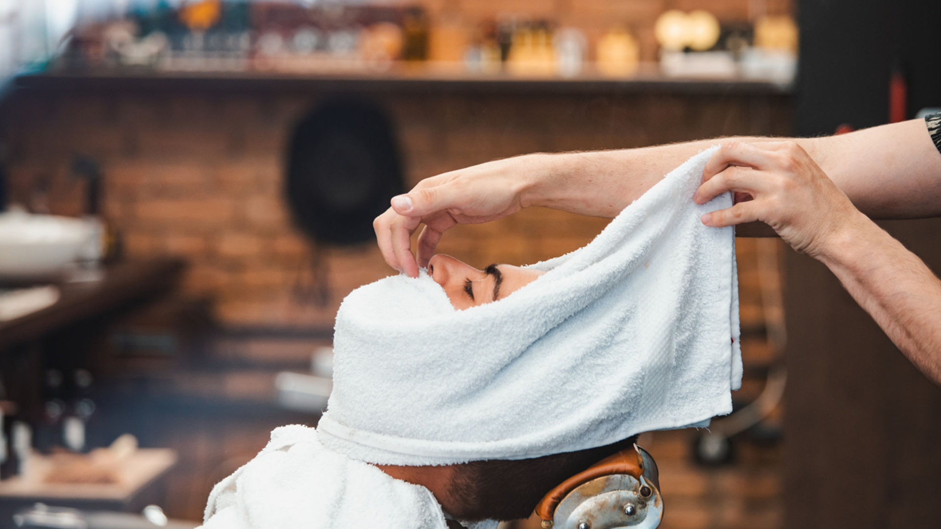 Man receiving hot towel treatment in barbershop.