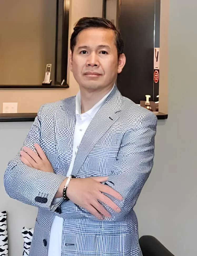 Confident man in a light gray blazer with arms crossed indoors.