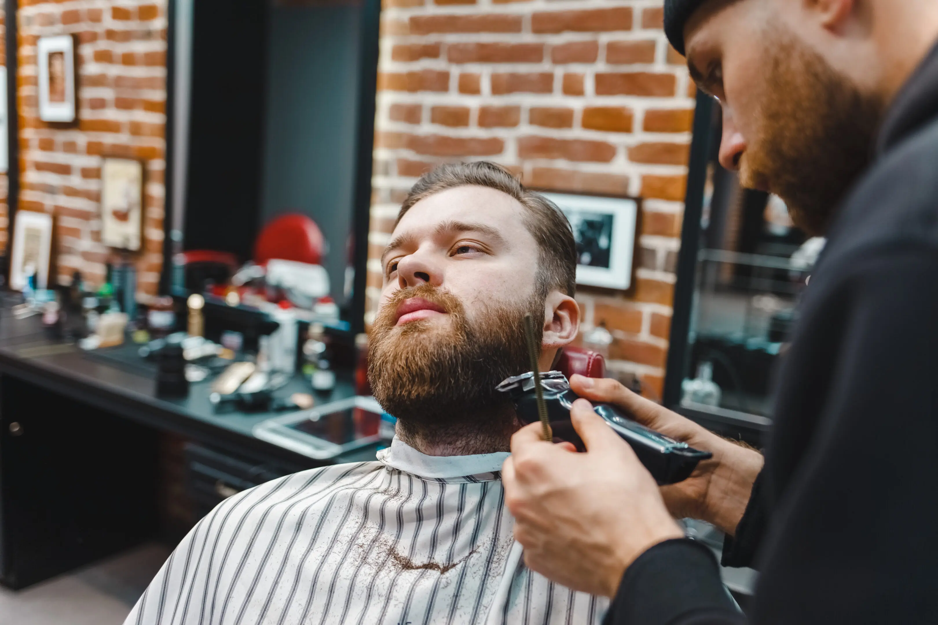 Barber trimming a man's beard in a stylish barbershop.