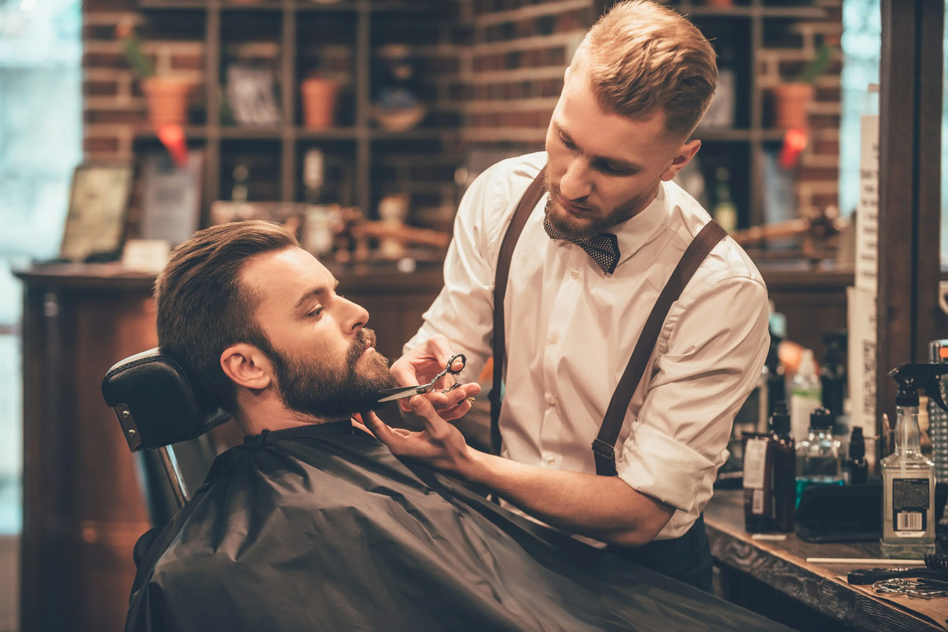 Barber carefully trimming a client's beard in a cozy barbershop.