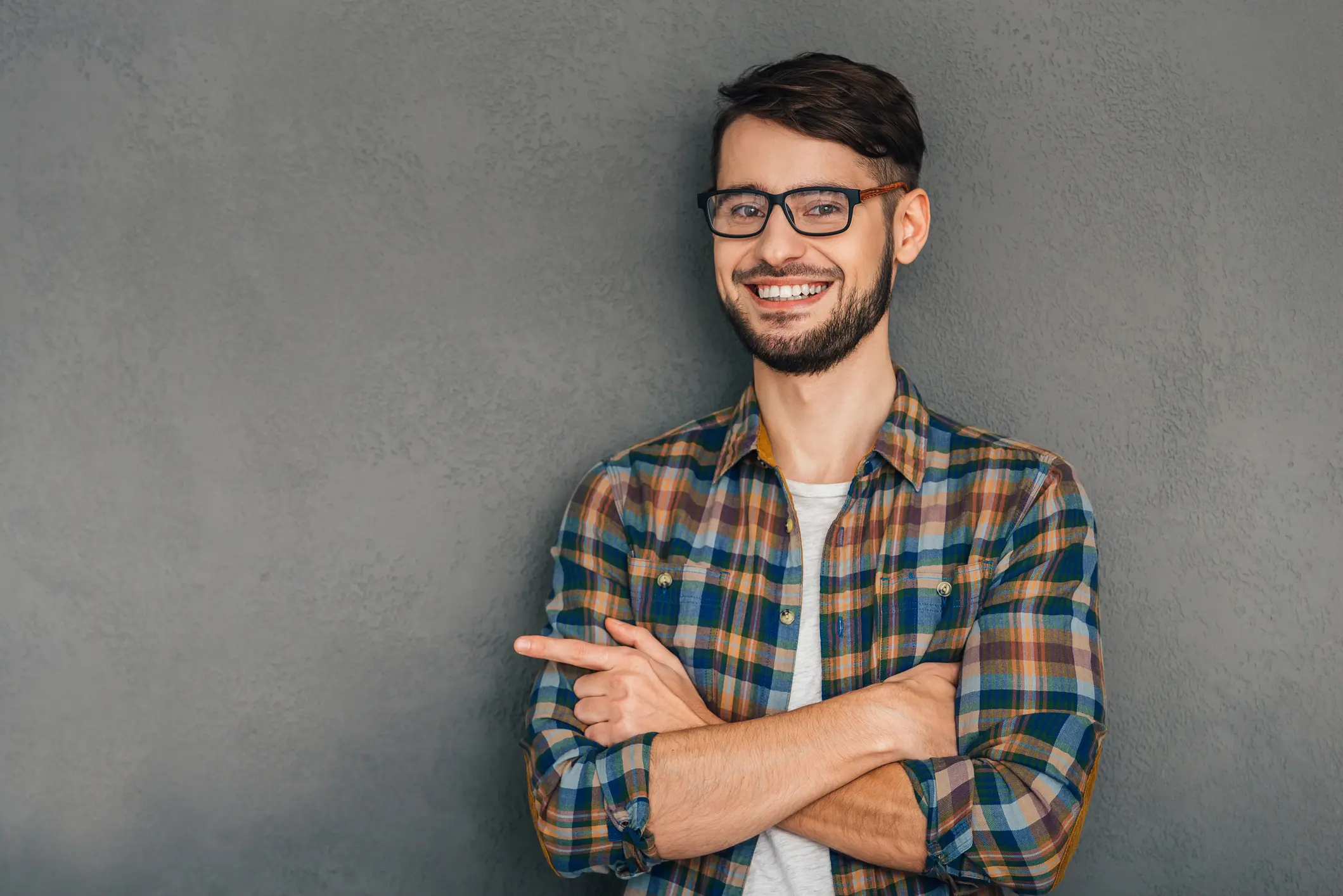Smiling young man in glasses and plaid shirt pointing to the side.
