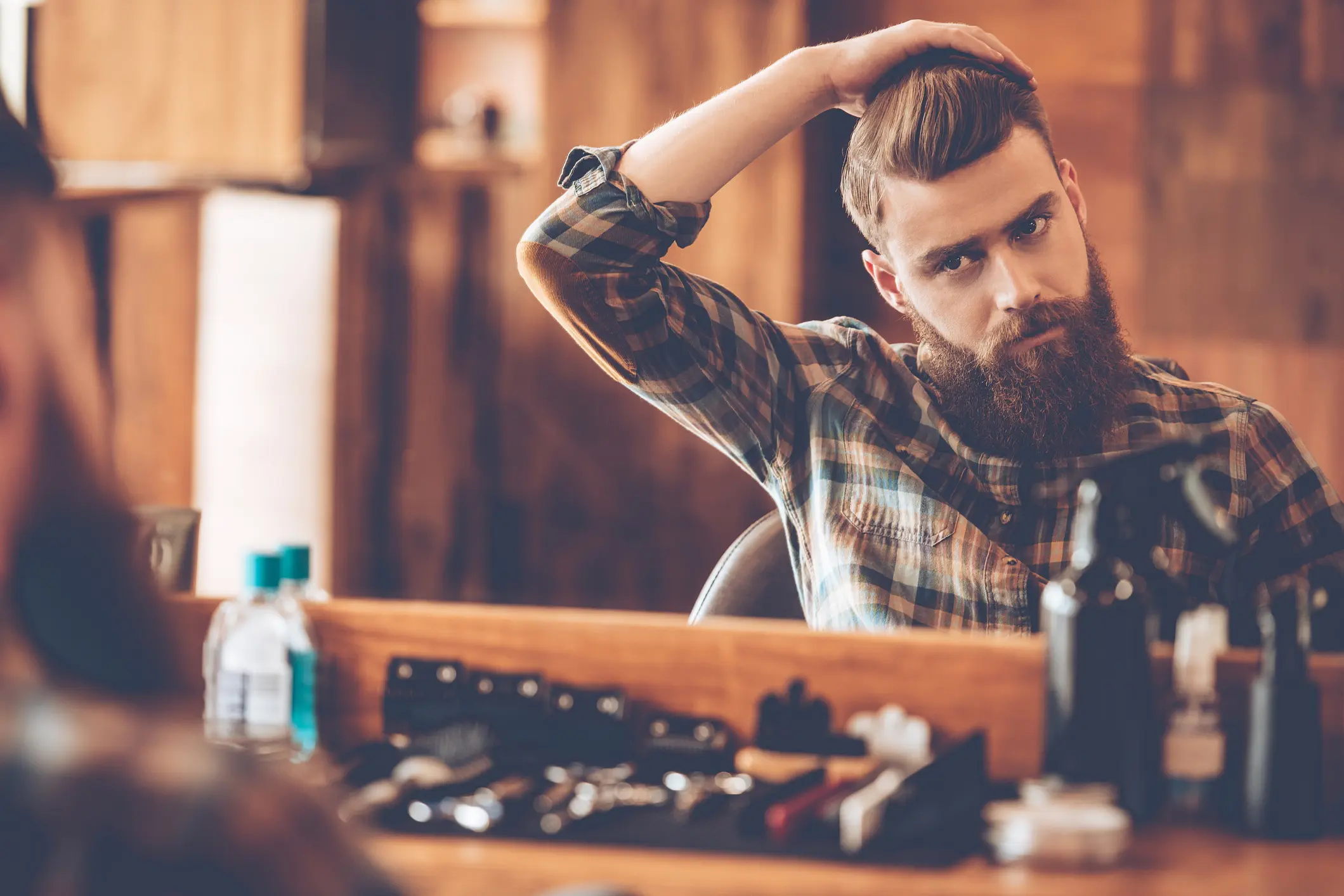 A bearded man styling his hair in front of a mirror.