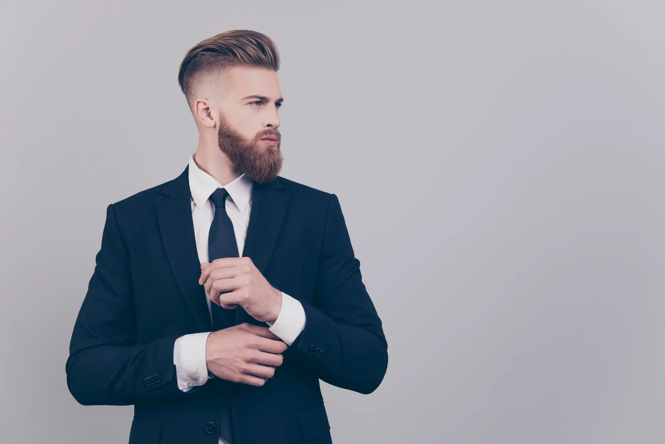 Man adjusting his suit and tie, looking to the side.